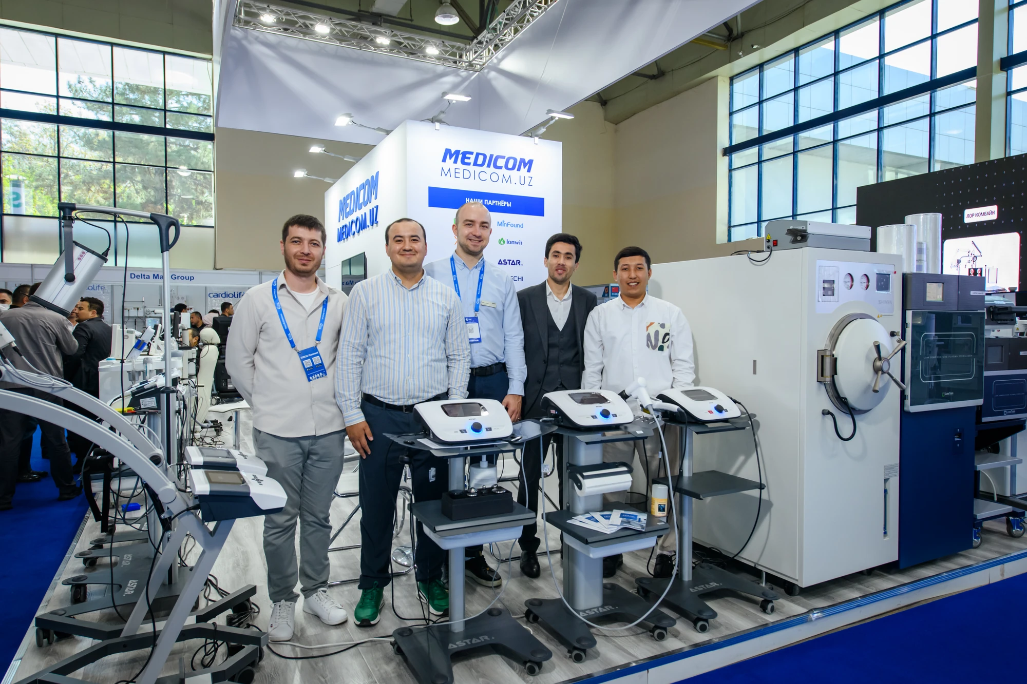 Команда MEDICOM на выставочном стенде рядом с физиотерапевтическим и стерилизационным оборудованием